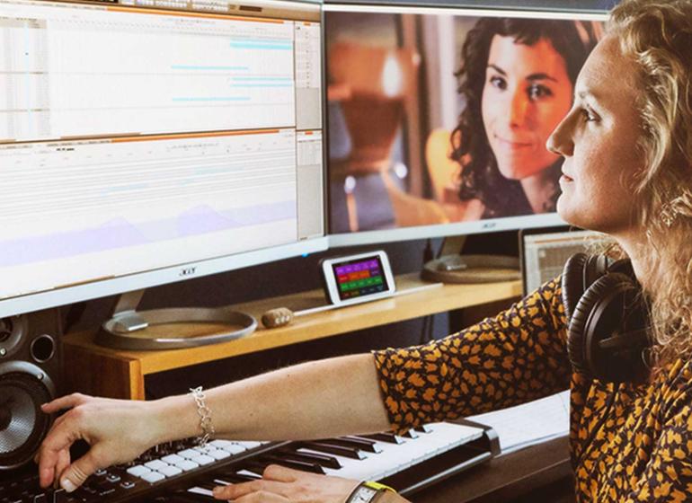 Musician scoring a film with a digital audio workstation open, alongside a second monitor that shows the film she is working on scoring.
