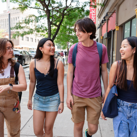 Four students walking down the street together, laughing